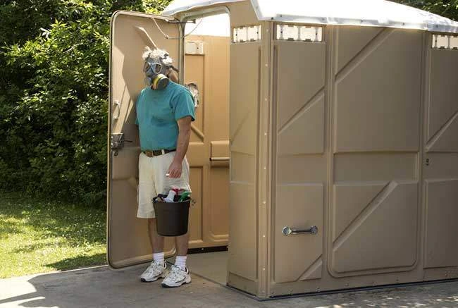Man in gas mask exiting large tan portable toilet - Common Bizarre and Disgusting Things Found in Porta Potties - ServiceCore Blog