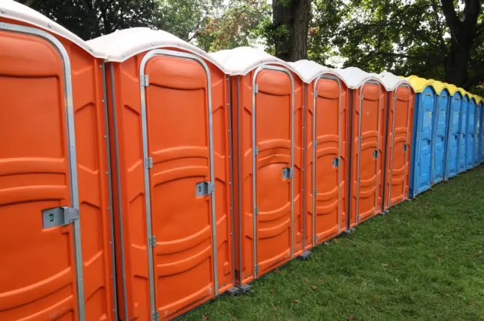 Row of orange and blue porta potties - History of the Porta Potty - ServiceCore Blog
