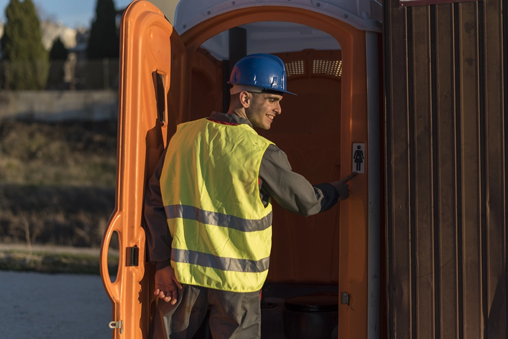Pumper entering orange portable toilet unit - How Many Toilets Do You Need to Start Portable Restroom Business? - ServiceCore Blog