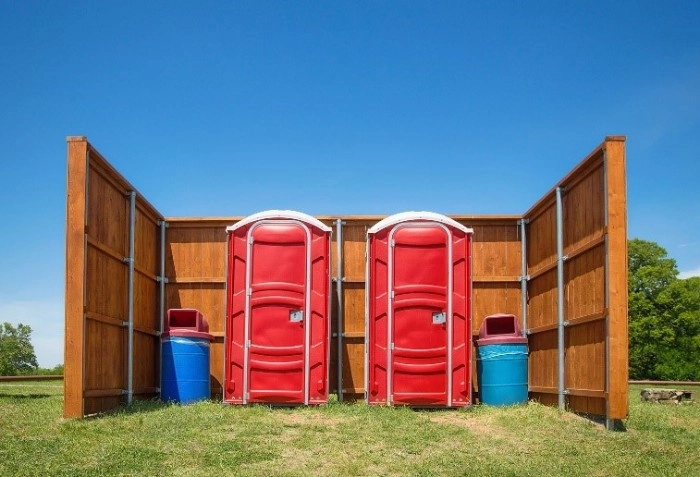 two red porta potties around fence - how to find porta potty contracts - ServiceCore software for portable restroom & dumpster companies
